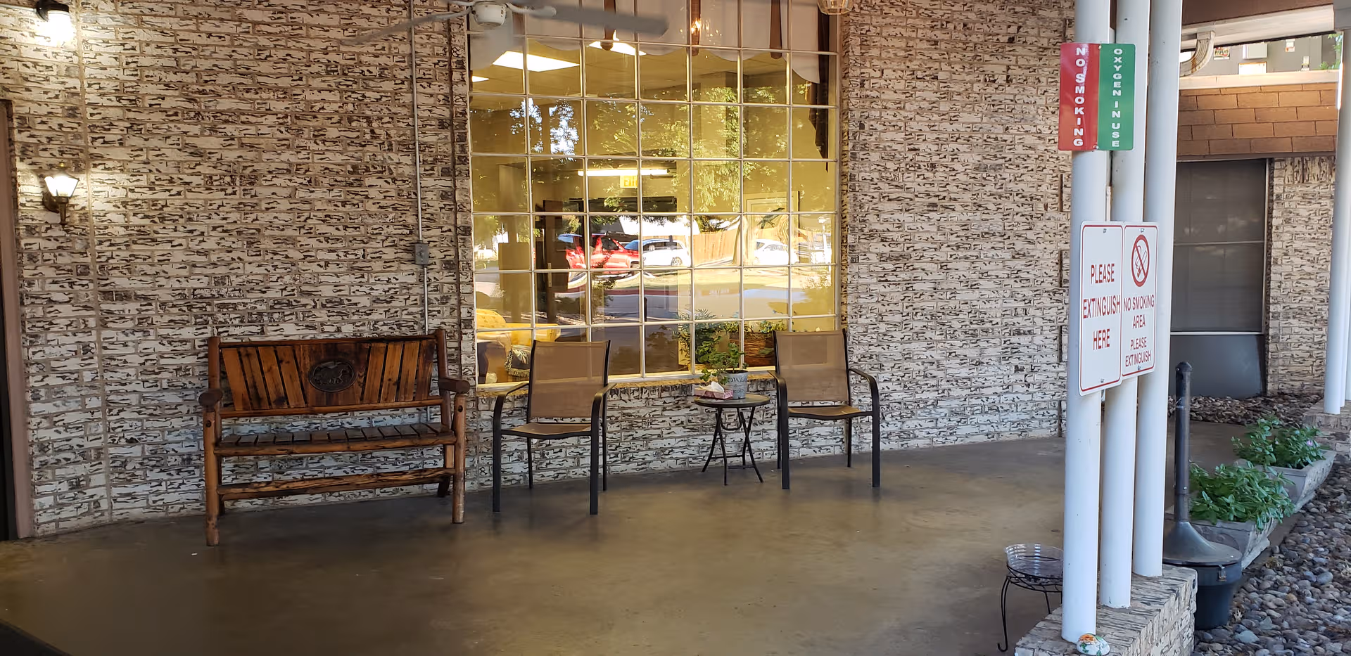 Exterior seating area in front of a stone-walled building with bench and chairs.