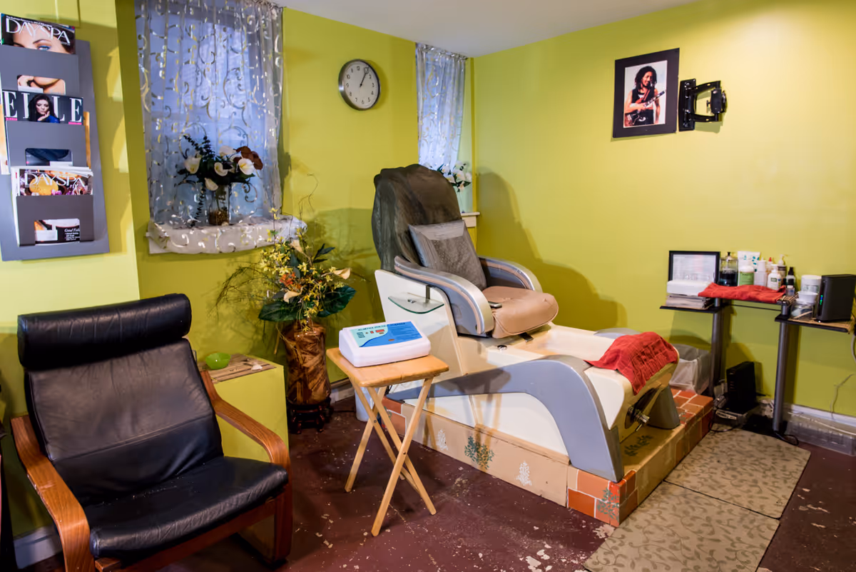 Lime-green interior featuring a pedicure chair, small table, magazines, and plants.