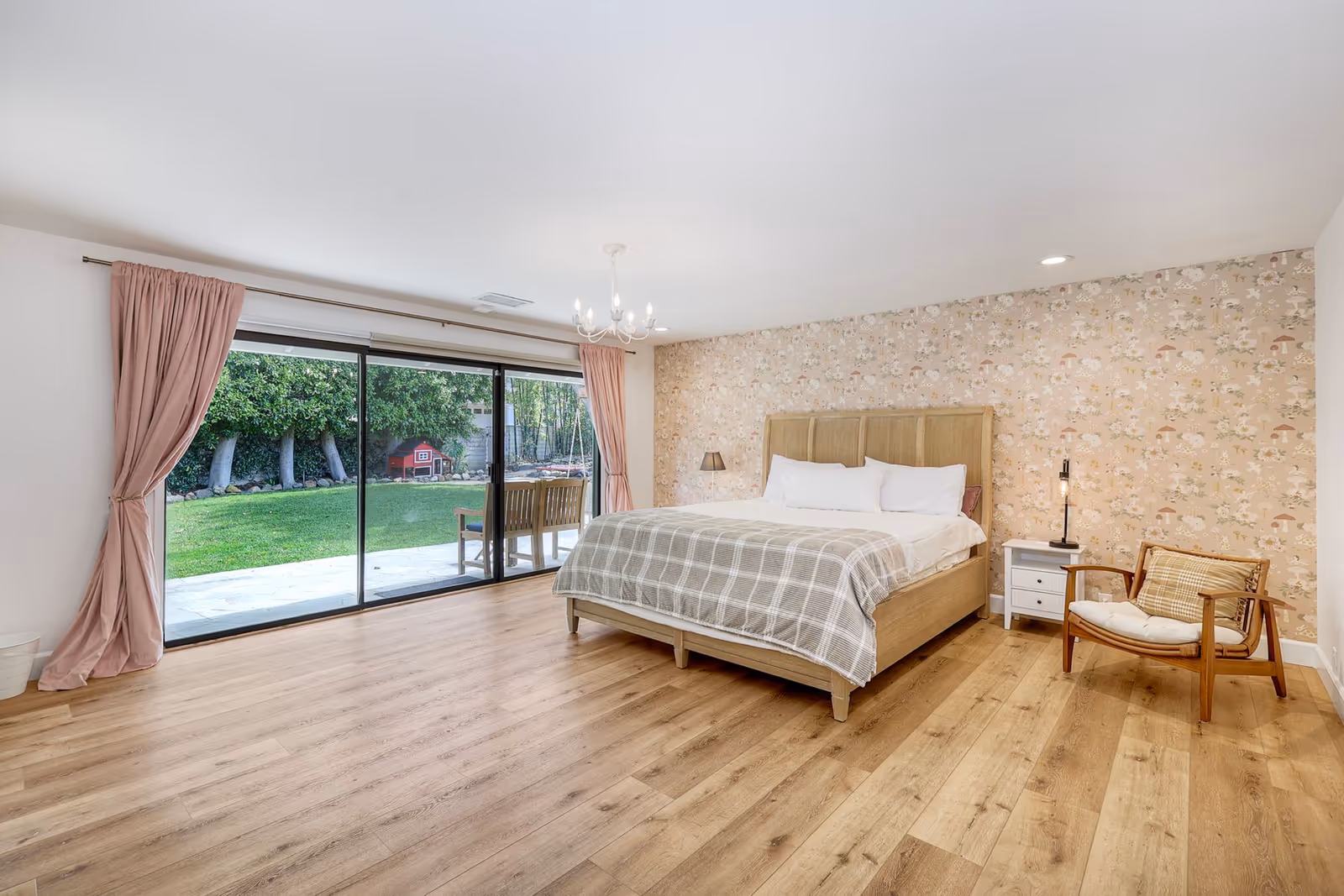 A spacious bedroom with a bed, floral wallpaper, and sliding glass doors to a green backyard.