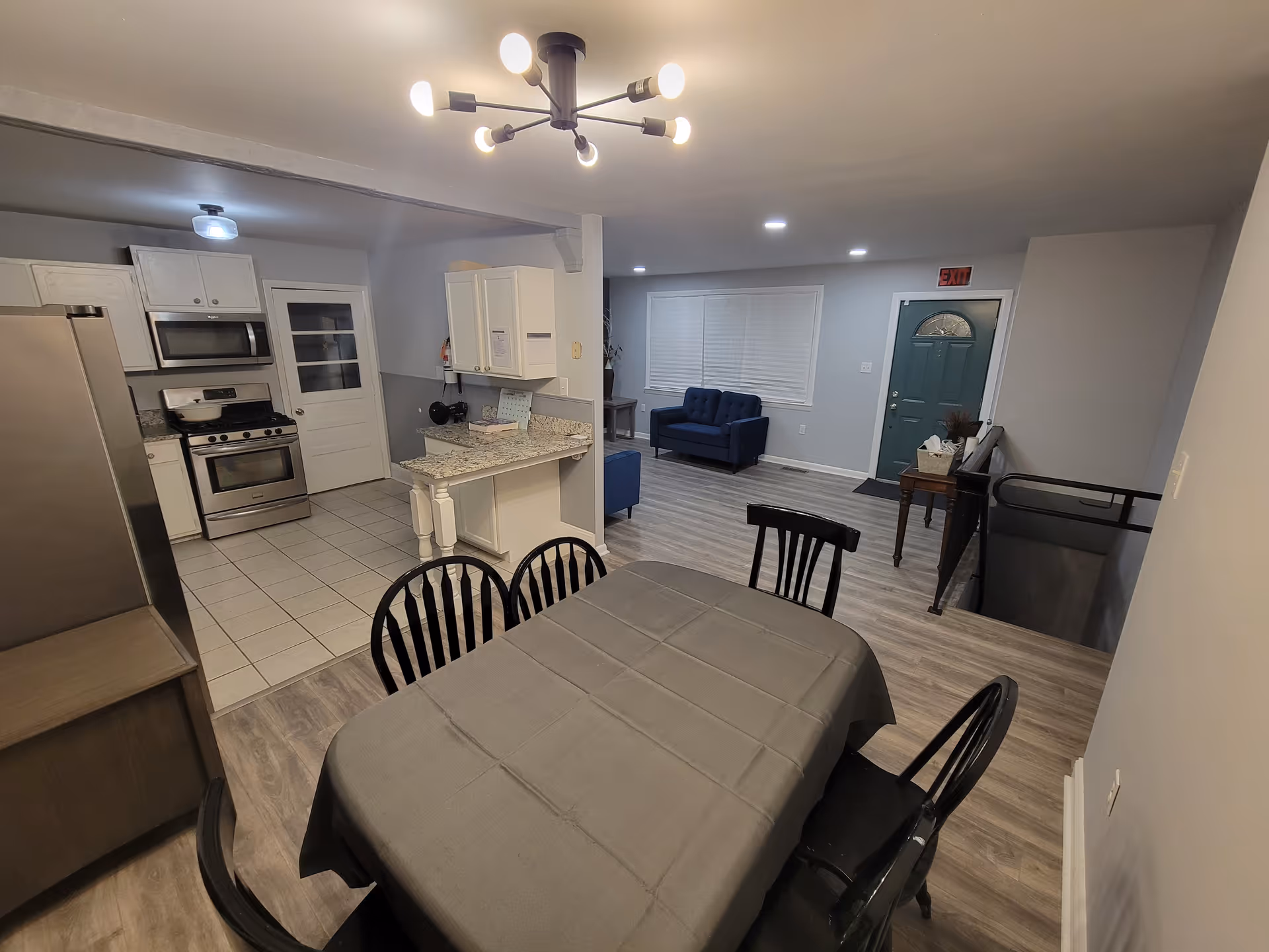Open concept kitchen and dining area with a gray table and blue seating in back.