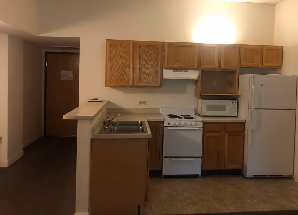 Apartment-style kitchen with wooden cabinets, sink, stove, microwave, and refrigerator.