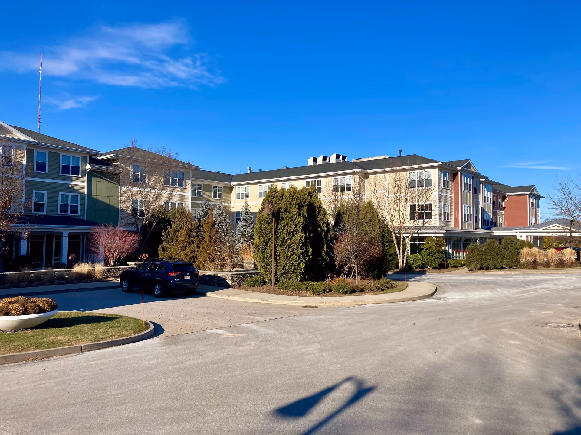 Front exterior of a multi-story senior living facility with landscaped driveway, a parked car, and a clear blue sky.