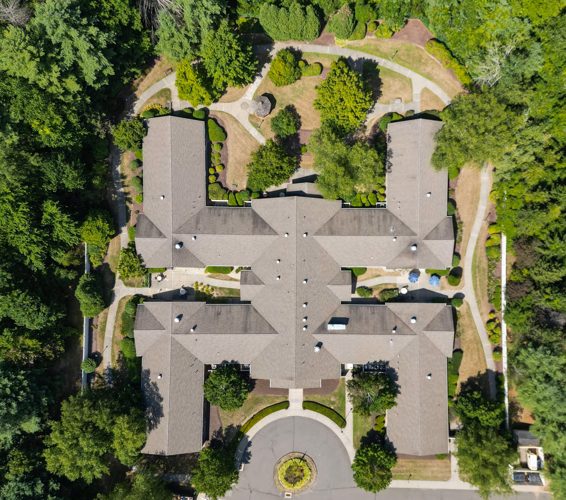 Aerial view of Arden Courts - ProMedica Memory Care Community (Avon) showing the building's roof, surrounding trees, landscaped gardens, walking paths, and a circular driveway entrance.