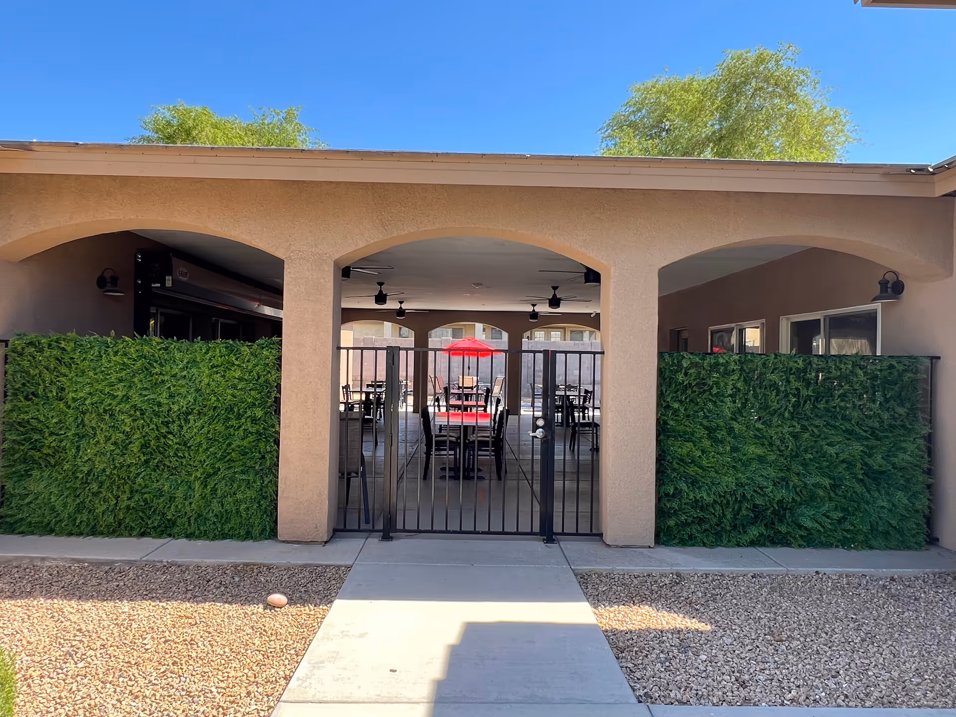 Gated outdoor patio with arched stucco walls, hedges, and seating area.
