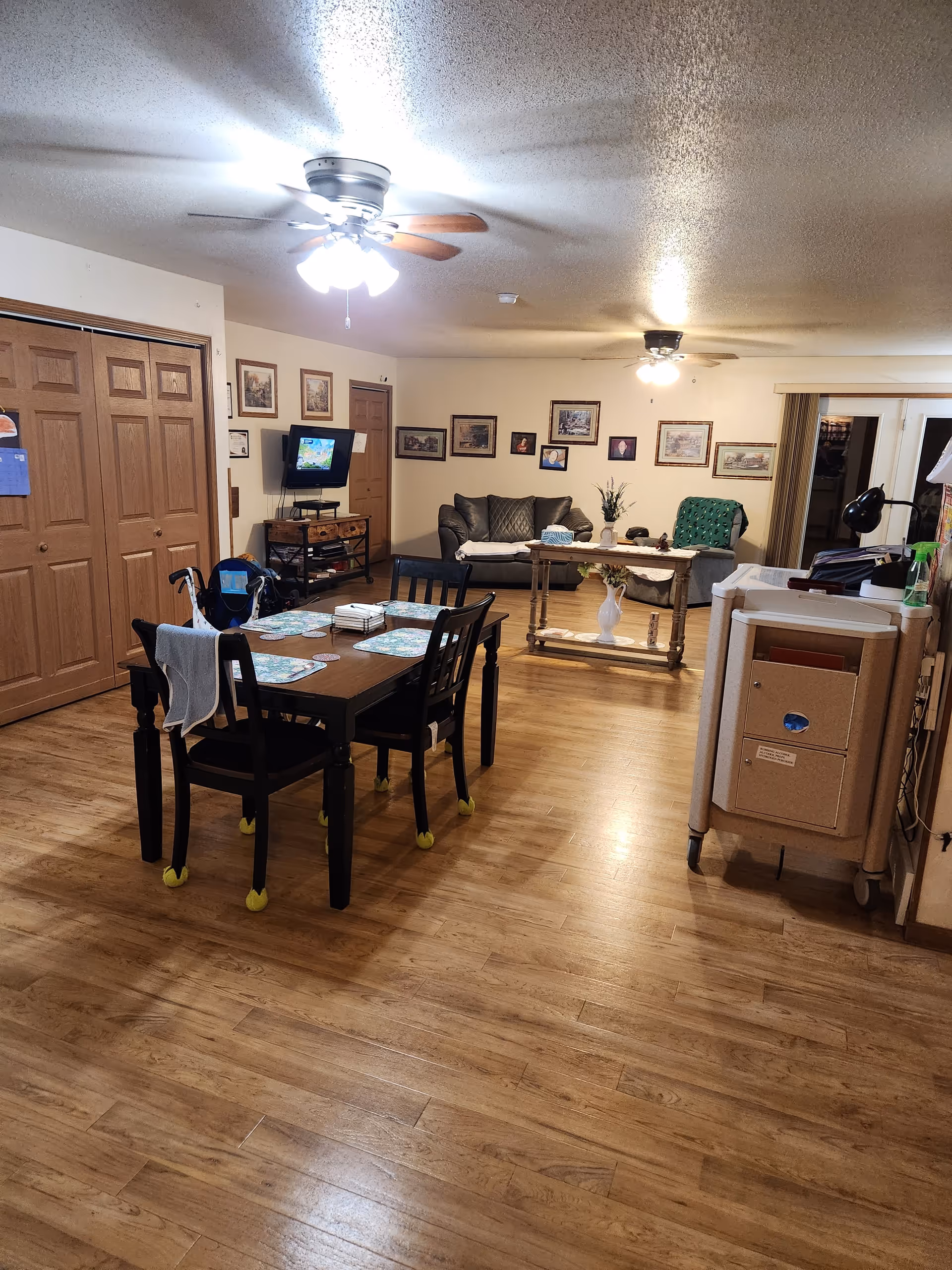 Cozy senior living common area with dining table, chairs, sofa, and wall decor.