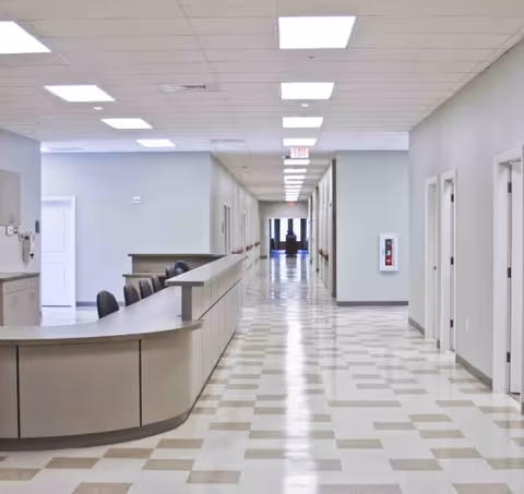 Long, well-lit hallway of a senior living facility with a curved reception desk on the left.