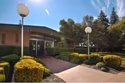 Exterior view of Windsor Elk Grove Care and Rehabilitation Center entrance with walkway and trimmed shrubs.