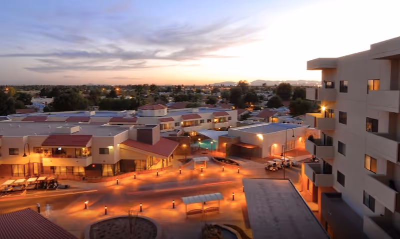 Aerial exterior view of the Friendship Village senior living complex at dusk with multiple buildings, a lit central courtyard, and walkways.