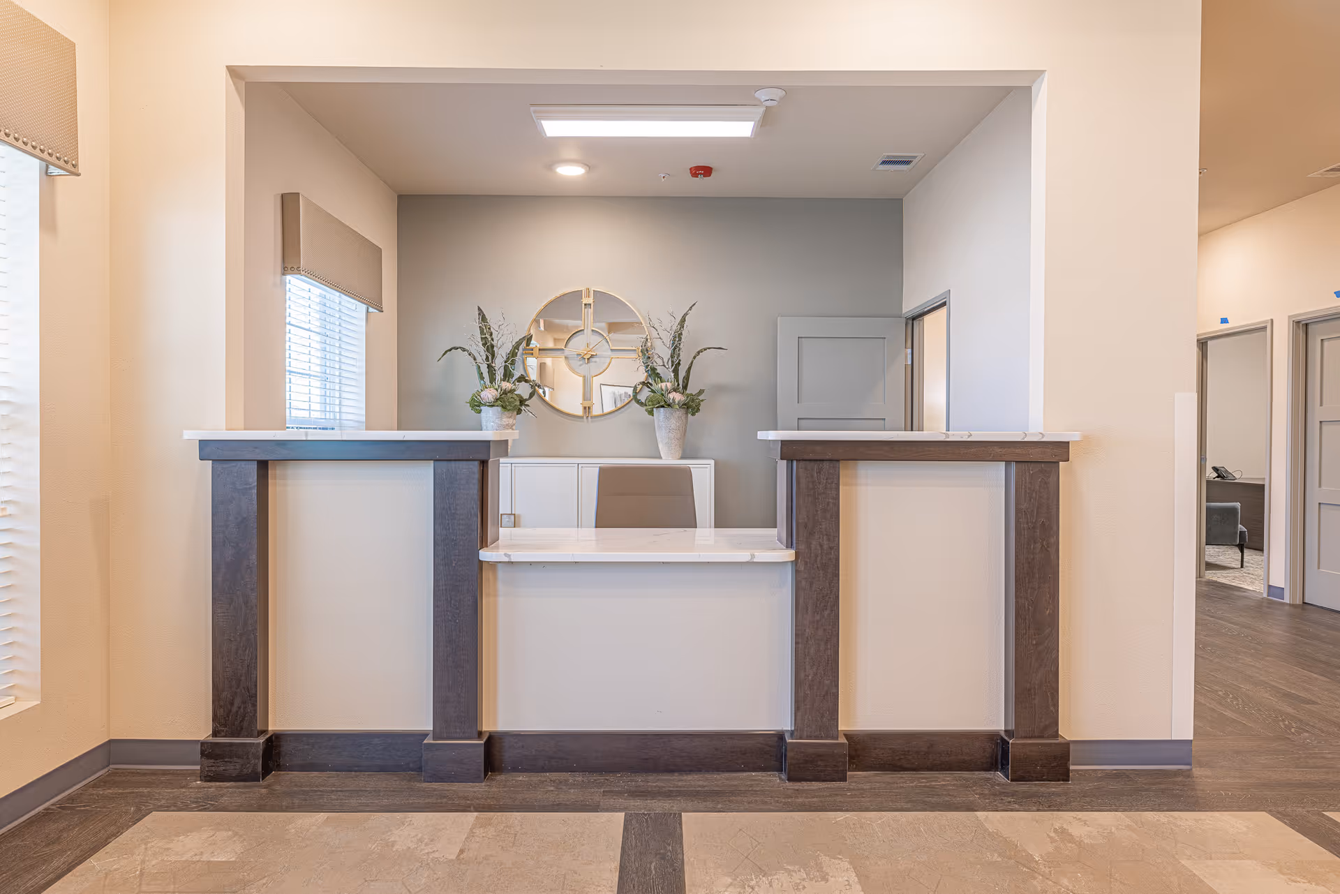 Reception desk inside a senior living facility, with plants and a round wall mirror.