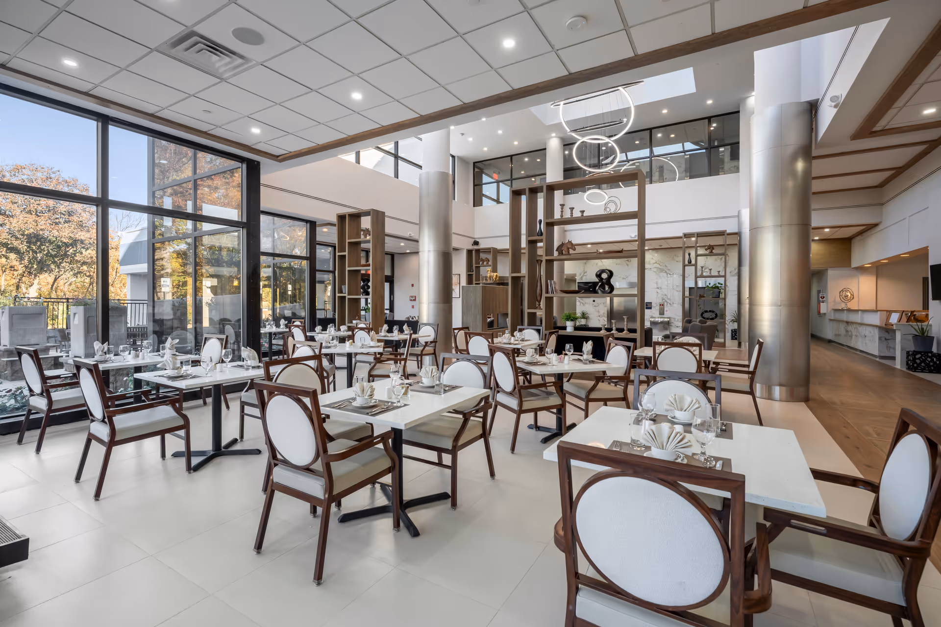 Bright, modern dining hall with arranged tables, chairs, and large floor-to-ceiling windows.