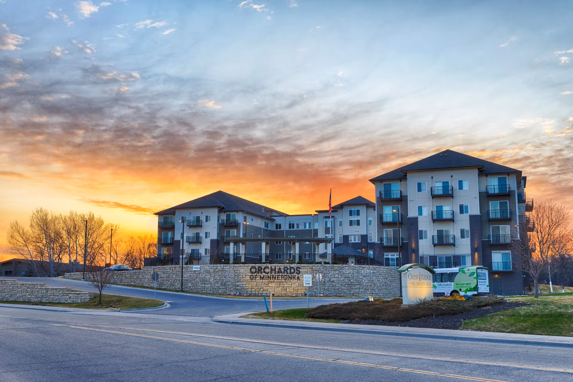 Exterior view of Orchards of Minnetonka Senior Living building at sunset, with stone wall sign.