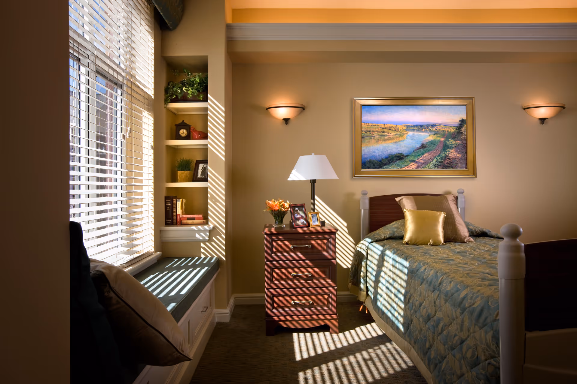A sunlit bedroom with a bed, nightstand, built-in shelves, and window blinds.