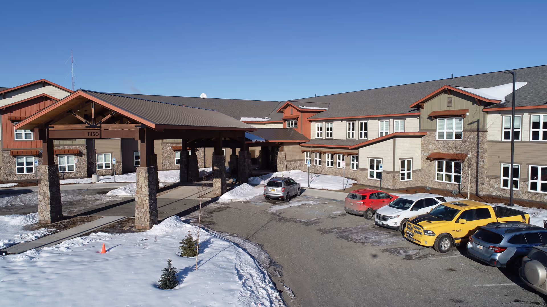 Exterior view of Maple Springs of Anchorage with a snow-covered parking lot and covered entrance.