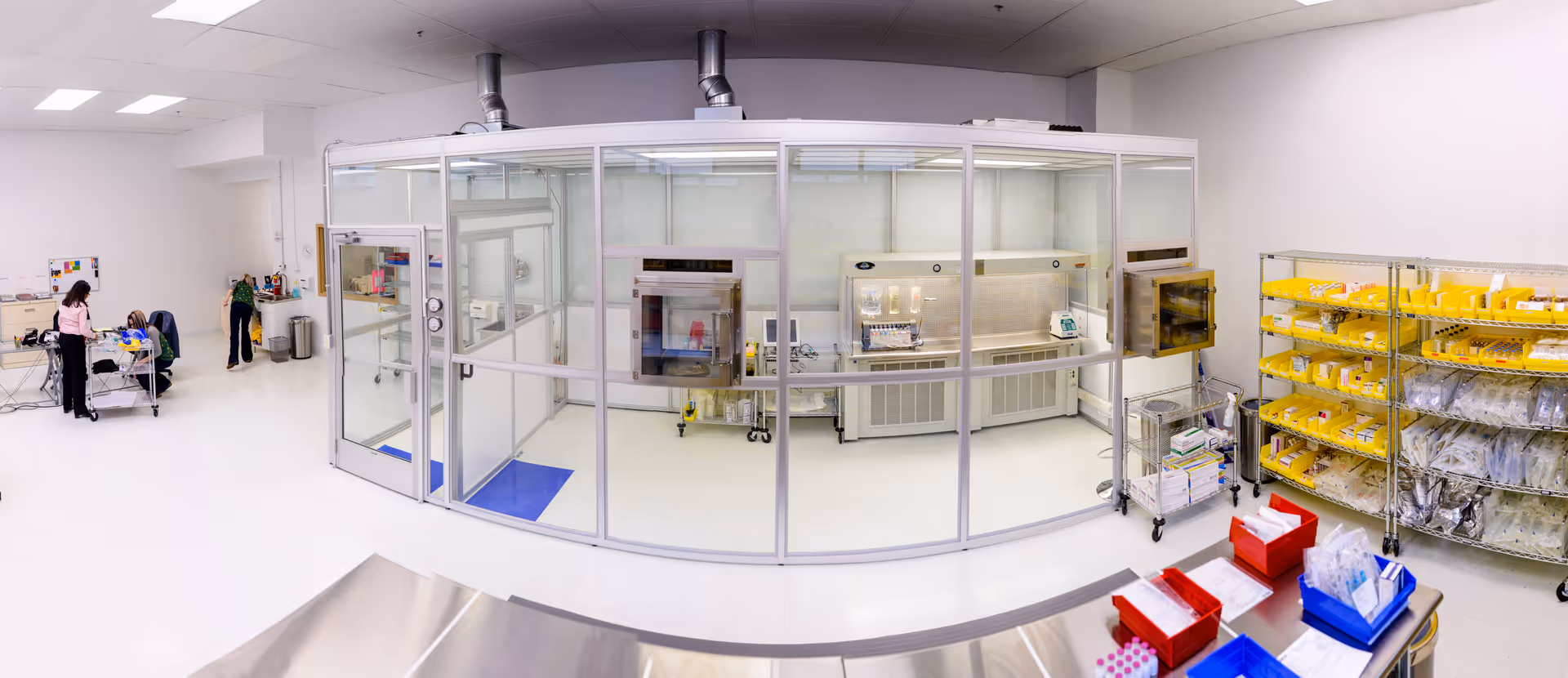 Bright clean room lab with glass enclosure, sterile cabinet, stainless surfaces, and yellow bin storage.
