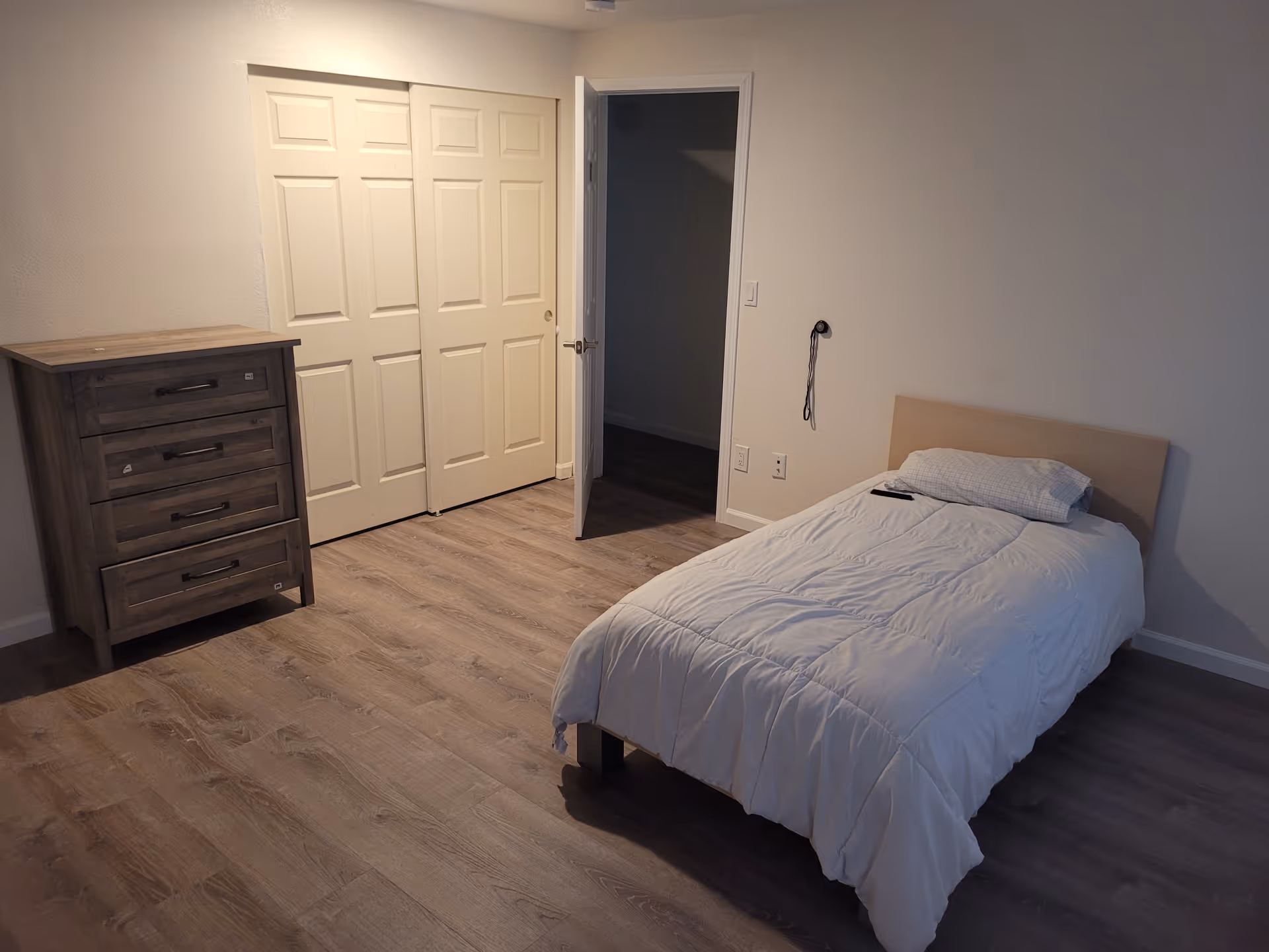 A simple bedroom with a single bed, dresser, and closet doors.