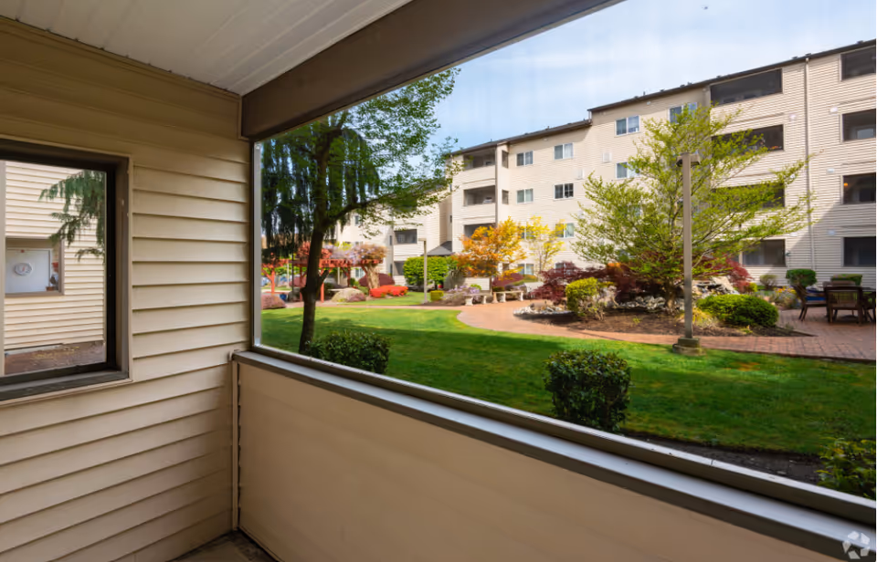 View from a covered patio or balcony overlooking a landscaped courtyard and multi-story apartment building.