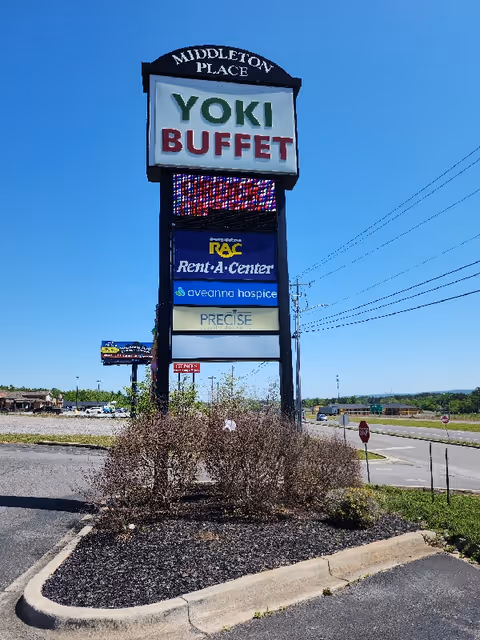 Tall outdoor signboard with multiple business names, including Aveanna Hospice, against a blue sky.