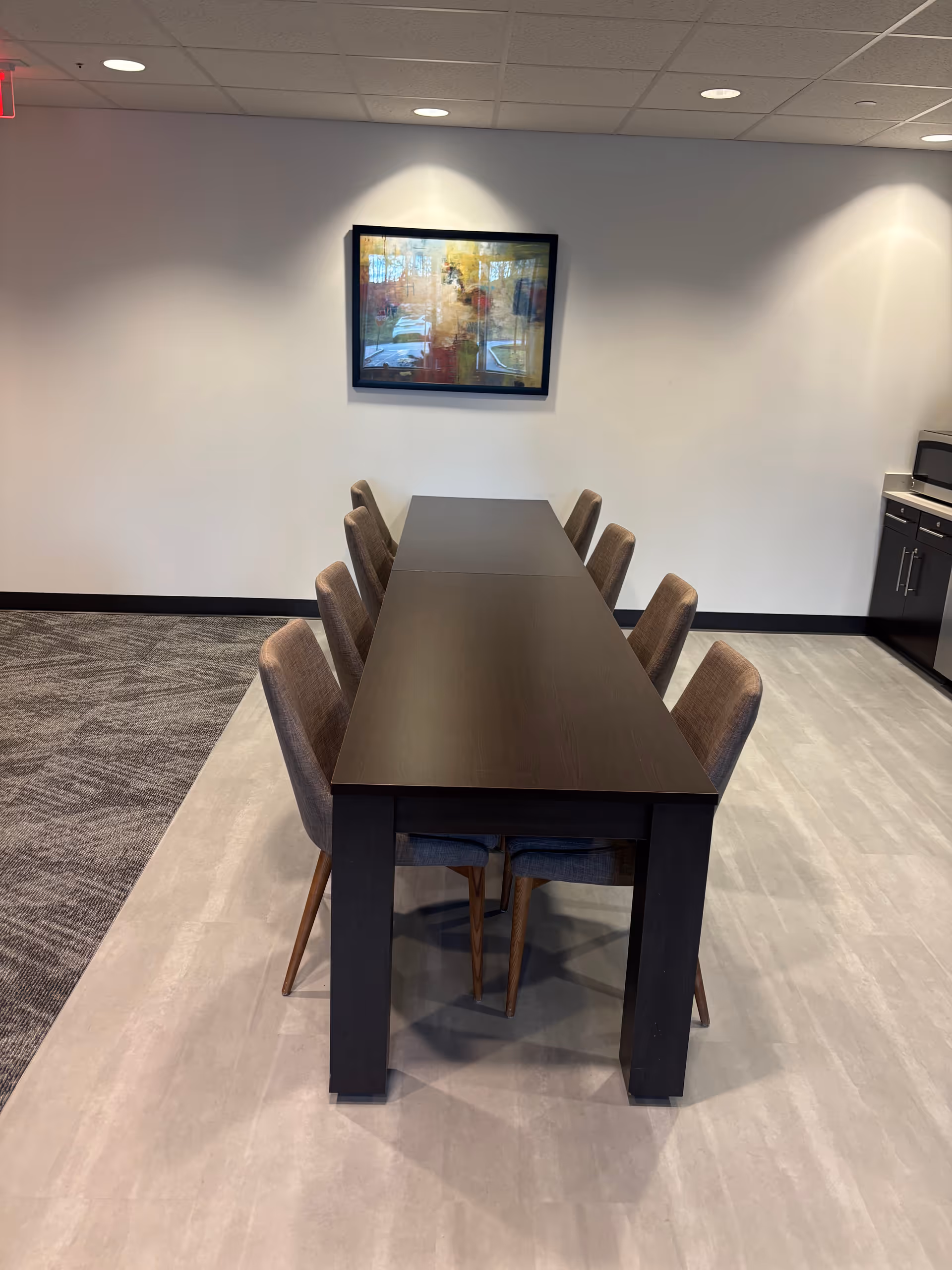 Long dark dining table with chairs in a modern facility dining area.