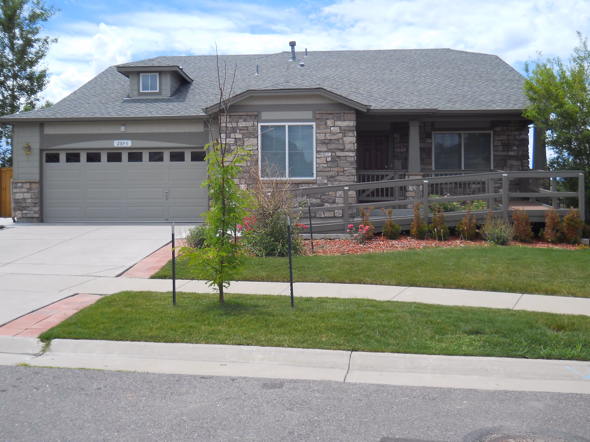 Front view of a senior living facility with stone facade, attached garage, and walkway.