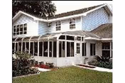 White, house-like senior living building with a glass-enclosed sunroom and manicured lawn.