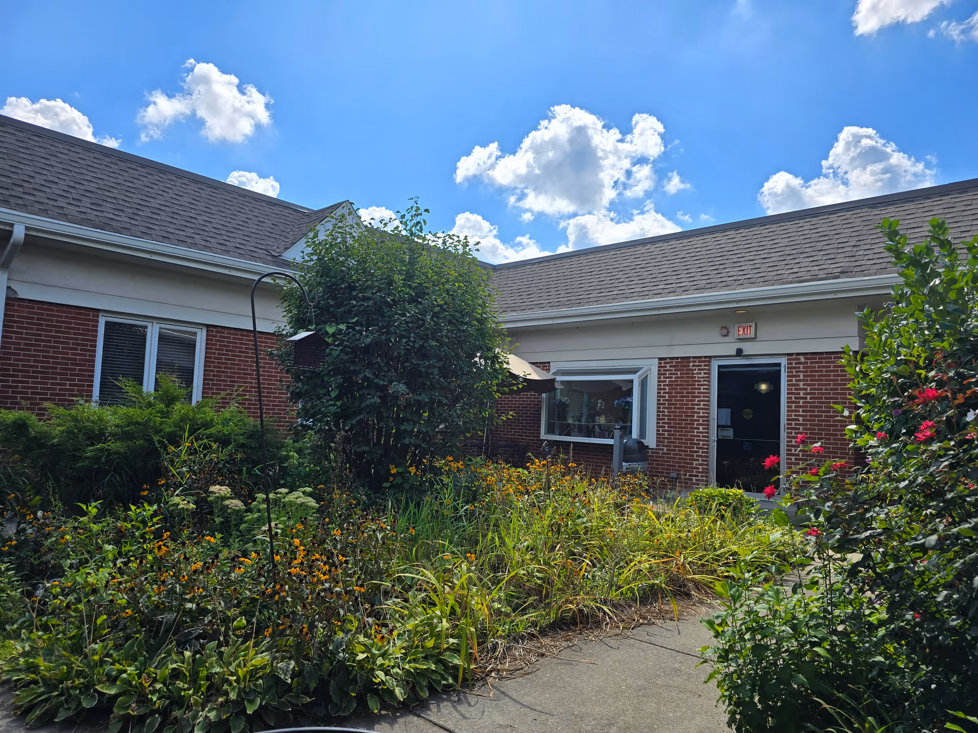 Brick senior living building with a garden in the foreground and a glass entry door.