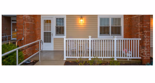 Front entrance of a senior living facility with beige siding, brick columns, and white railing.