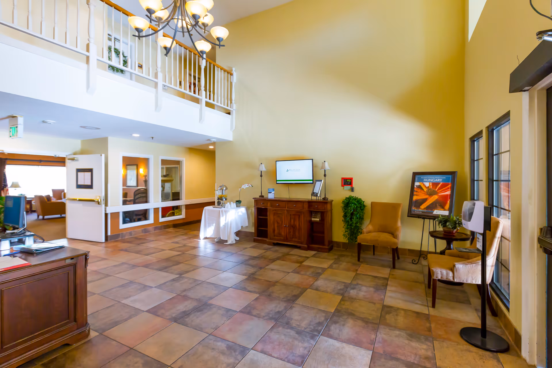 Bright lobby with reception desk, second-floor balcony, seating area, and a poster display.
