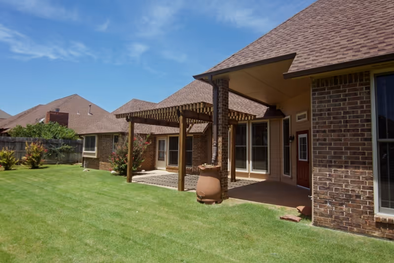 Brick senior living building with a covered patio and well kept green lawn.