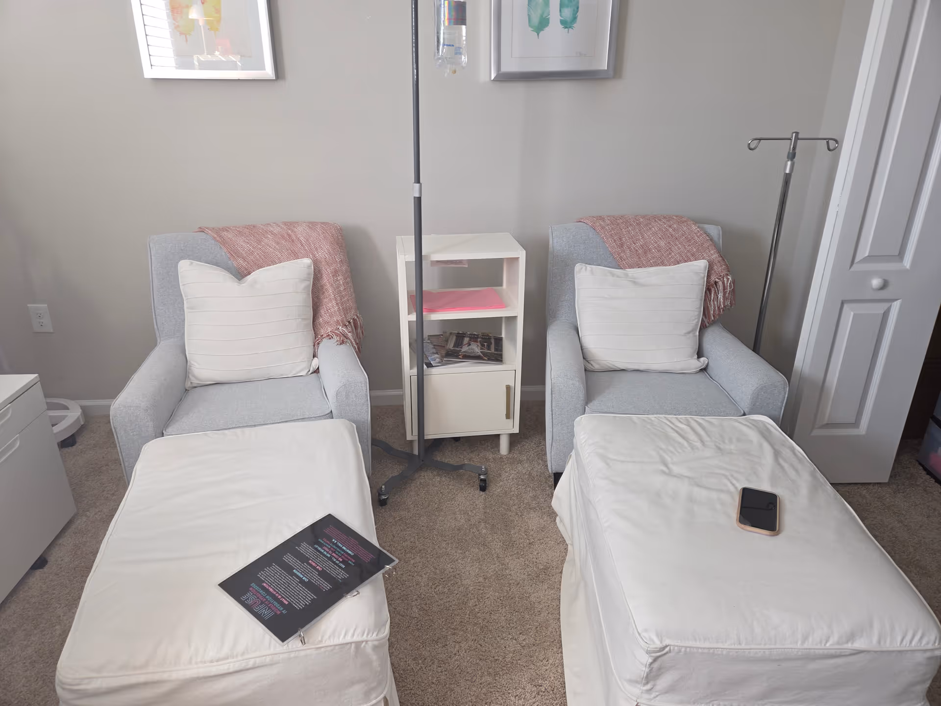 Two cushioned lounge chairs with white footrests face a small white cabinet in a clinical area.