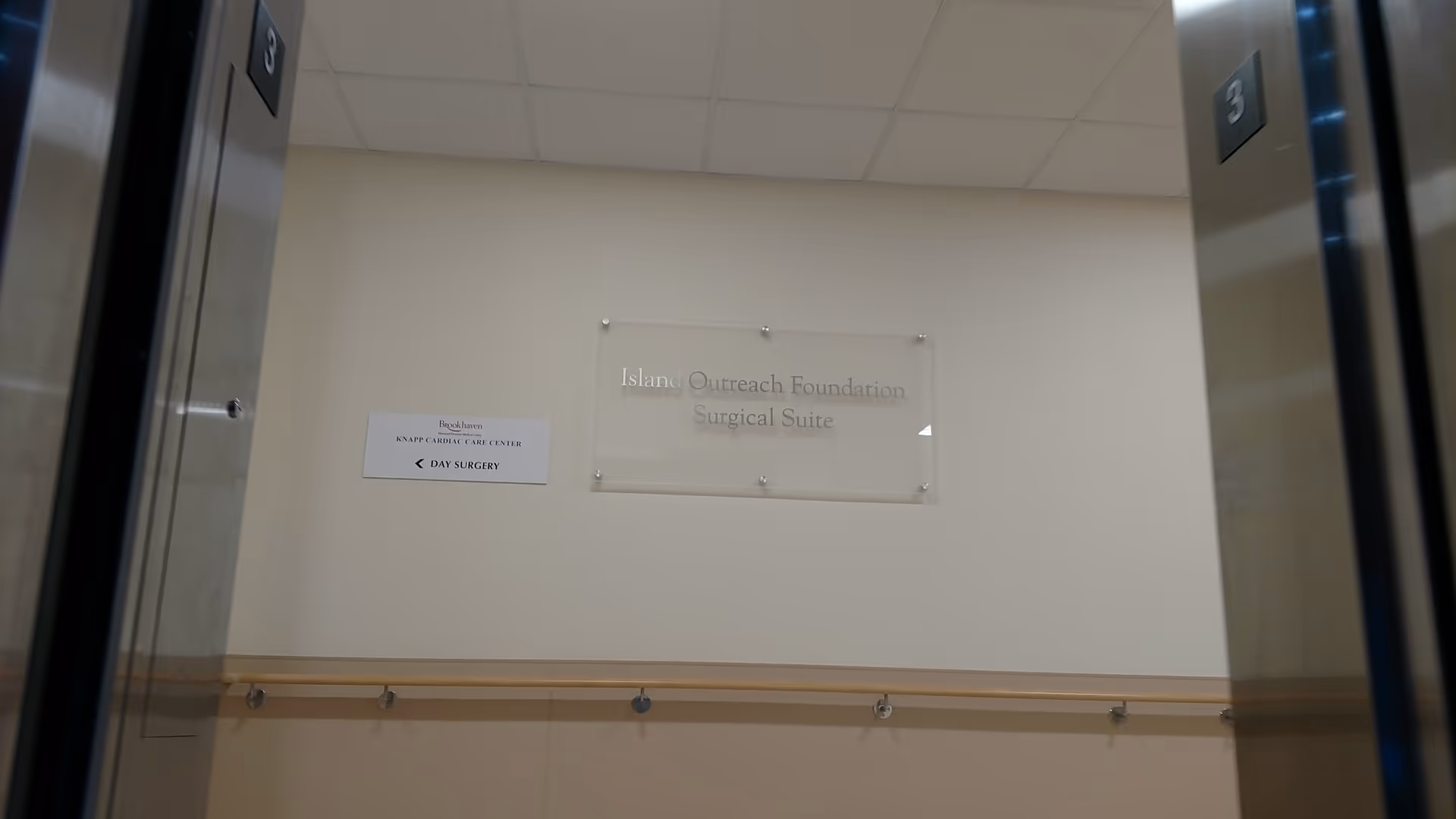 Elevator lobby inside a senior facility with wall signage and a wooden handrail.