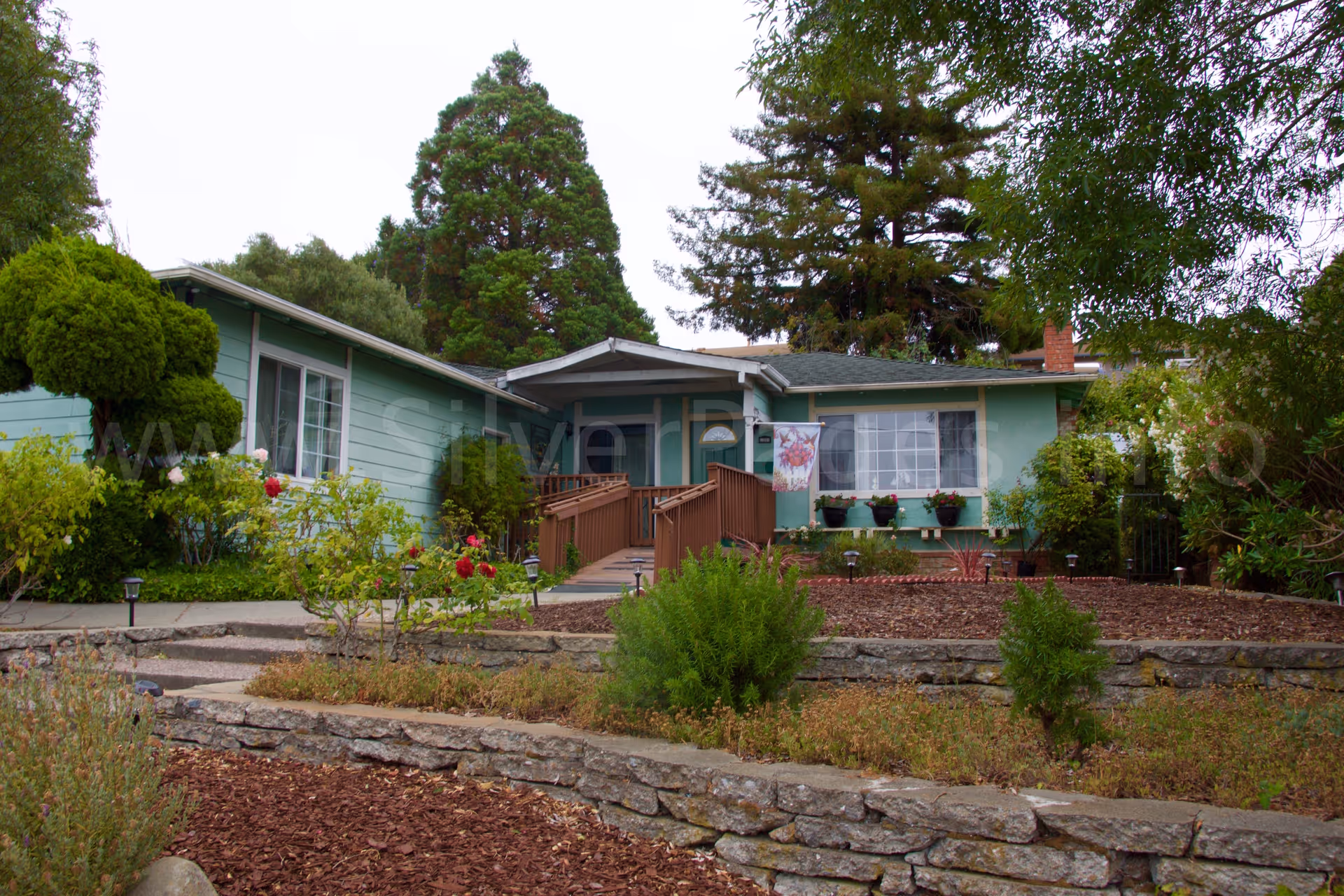 Green, single-story assisted living facility exterior with landscaped front yard and steps.