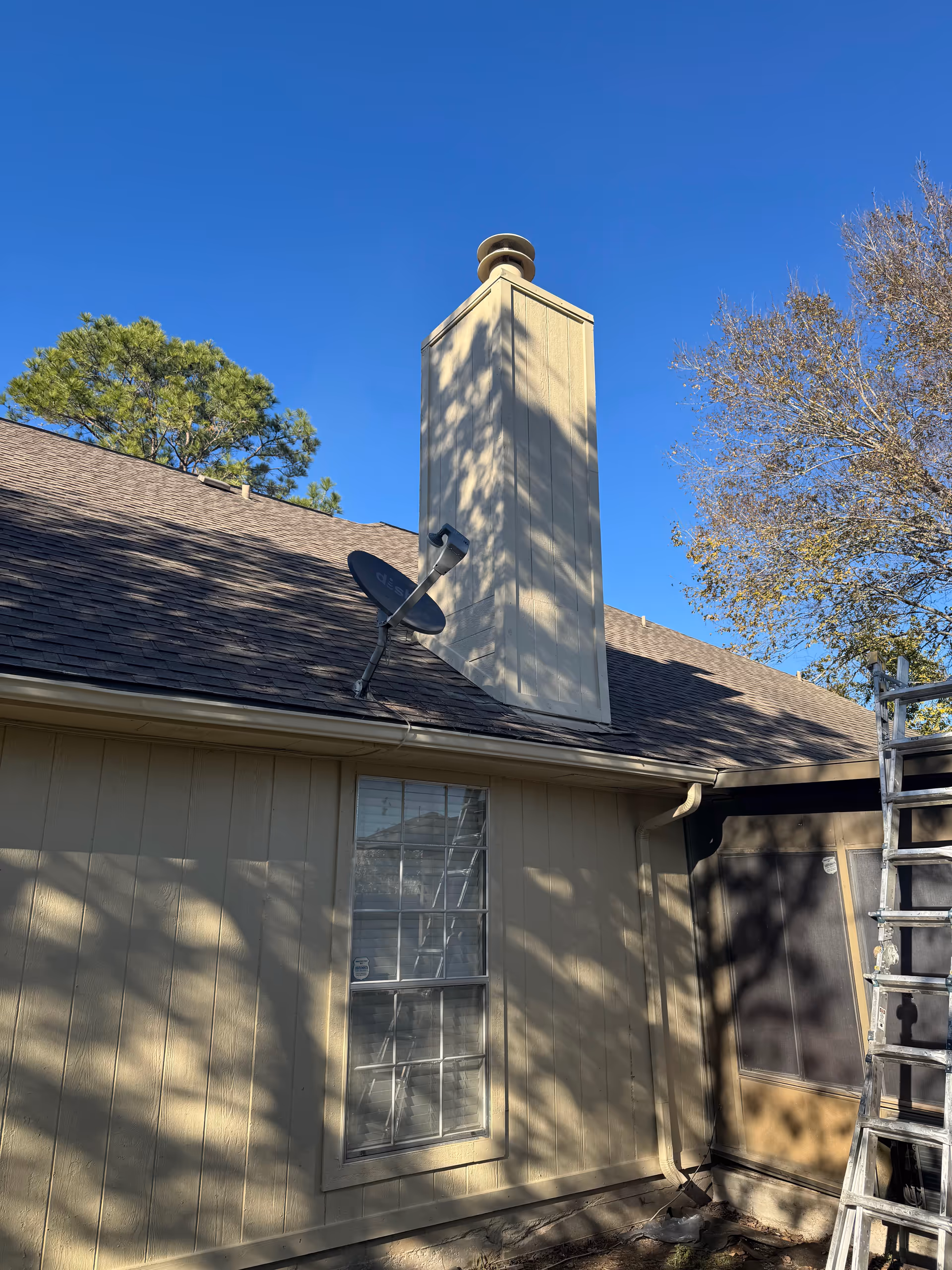 Beige single-story house exterior with a window, chimney, satellite dish, and a ladder.