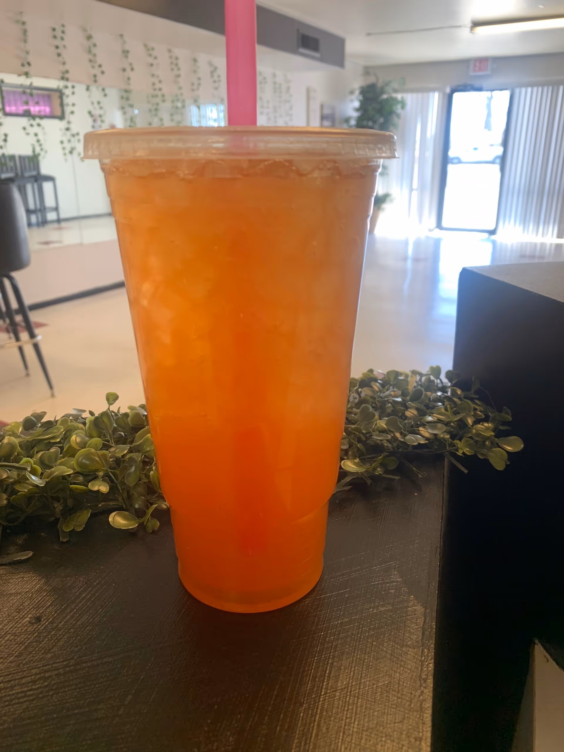 orange drink in a plastic cup with pink straw on a counter in a bright lobby.