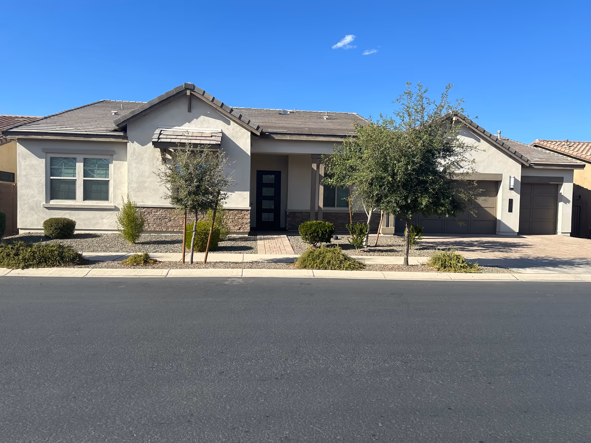 Front view of a single-story residential building with a driveway, two garages, and desert landscaping.