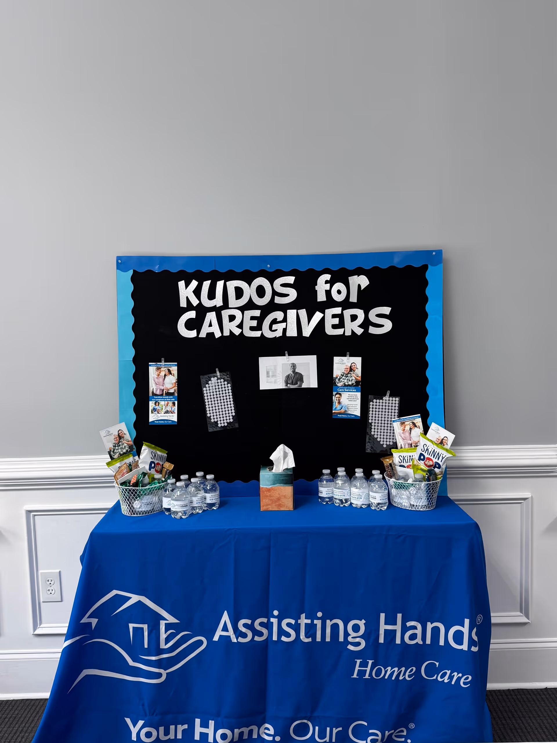 Indoor table display with blue banner and 'KUDOS for CAREGIVERS' bulletin board.