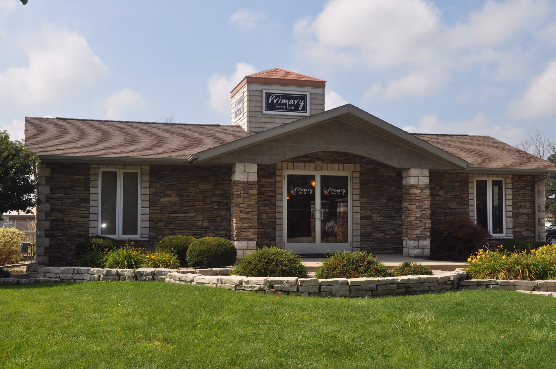 Front view of a stone-faced senior living building with entry doors and landscaped yard