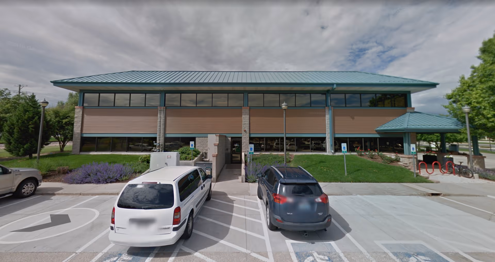 Modern, single-story building with teal roof, brick columns, and a front parking lot.