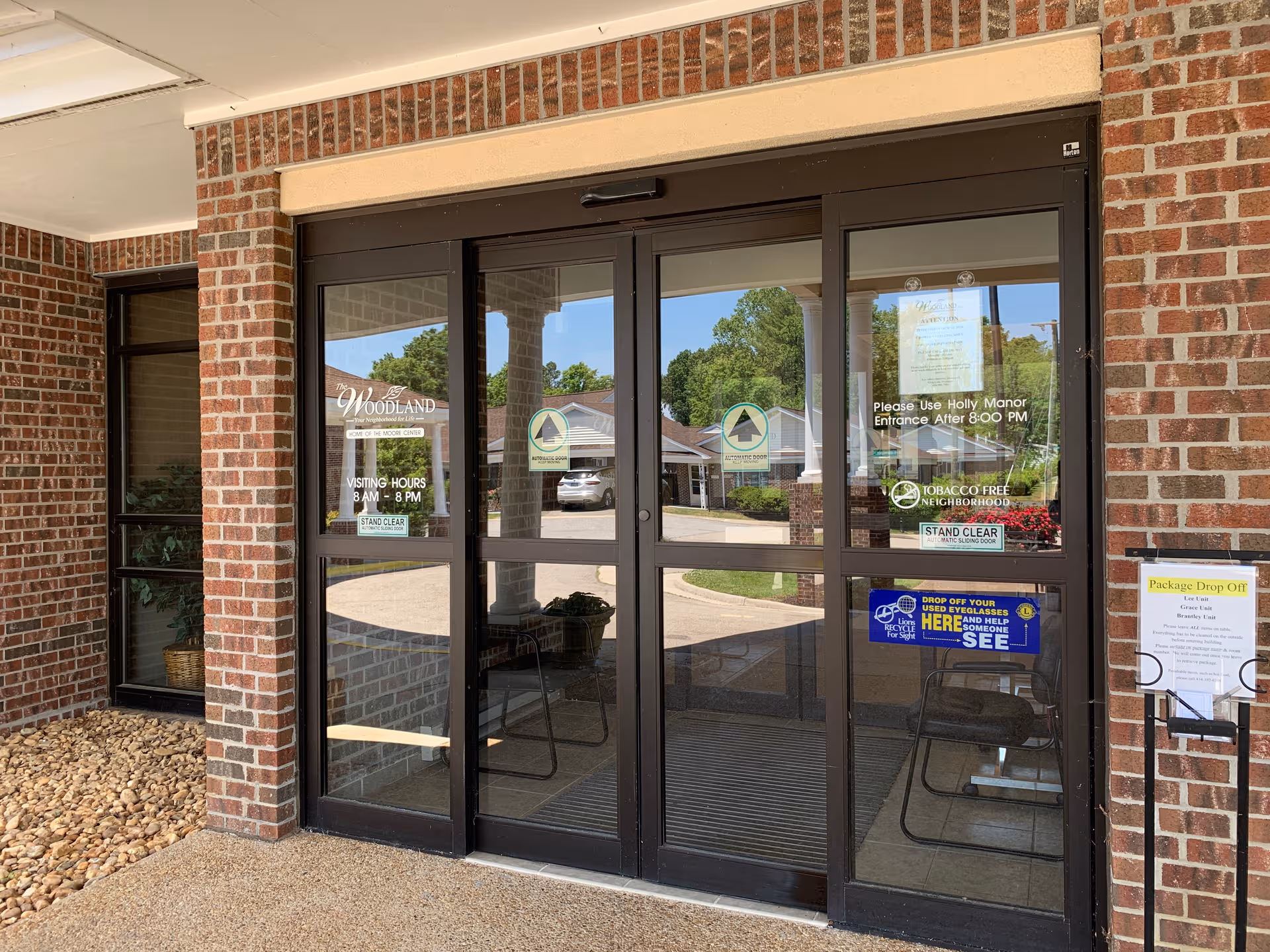 Brick exterior entrance with glass doors and signs for The Woodland senior facility.