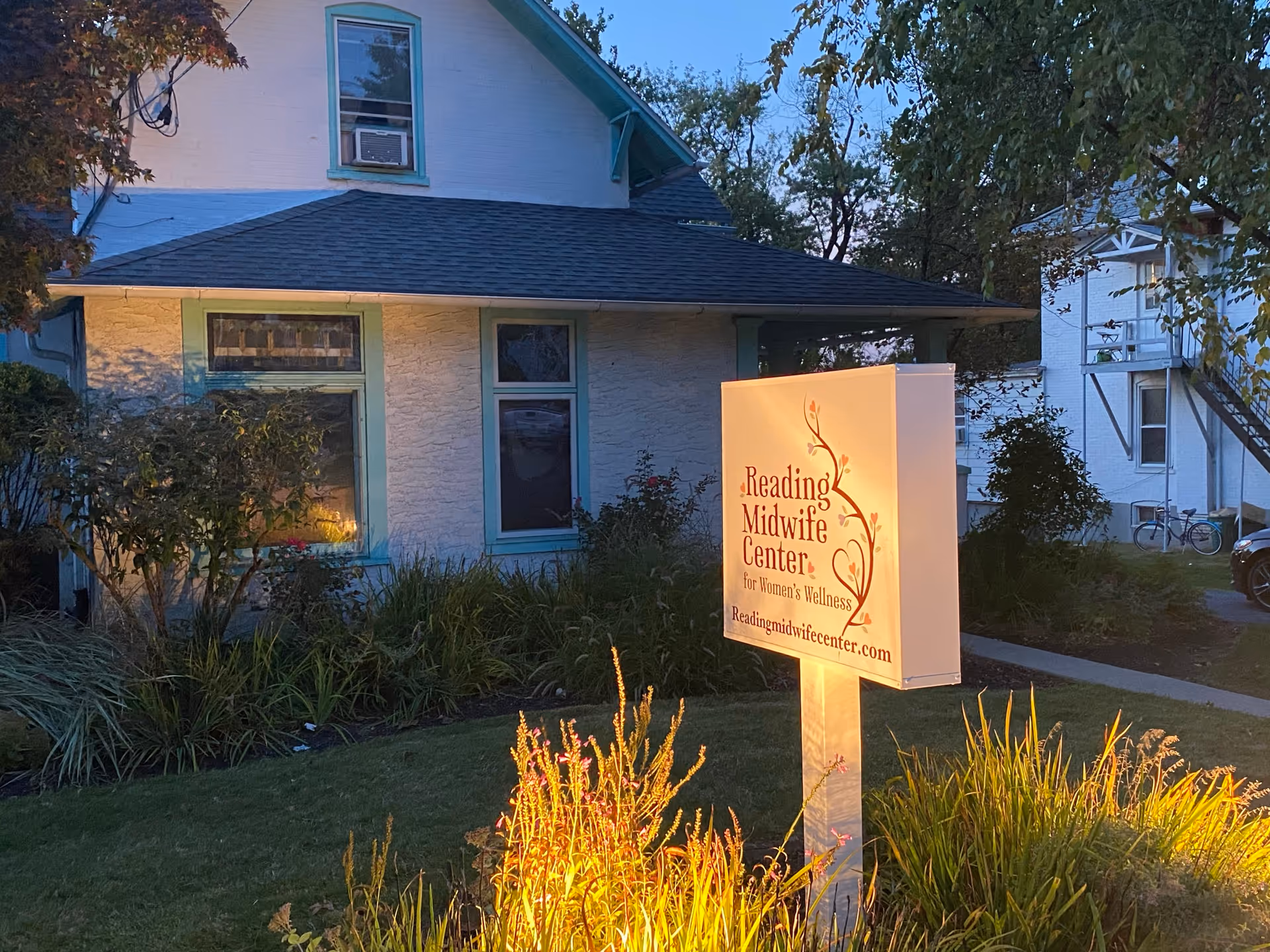 White cottage-style building with a lit sign for Reading Midwife Center for Women’s Wellness.