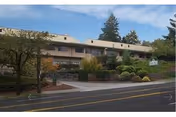 Two-story beige senior care building with manicured shrubs along a street.