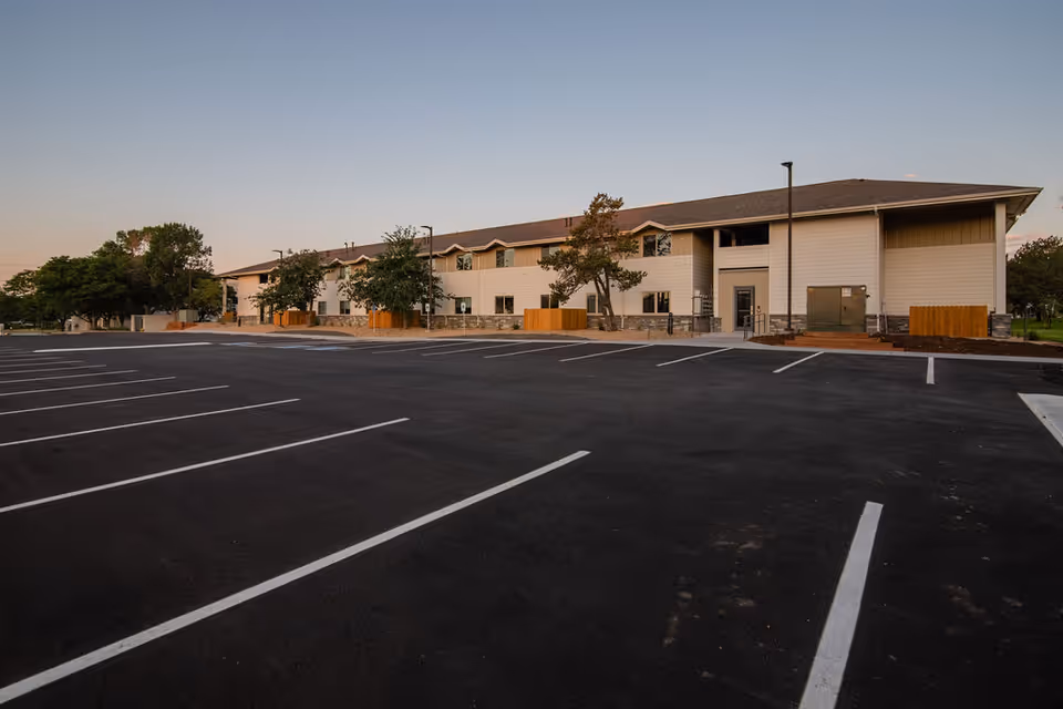 Exterior view of a senior living facility with a spacious parking lot in front.