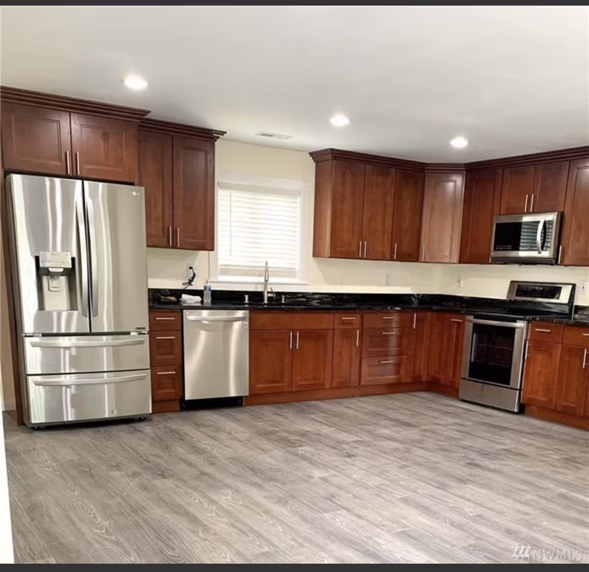 Modern kitchen with wooden cabinets, granite countertops, stainless steel appliances, and a window above the sink.