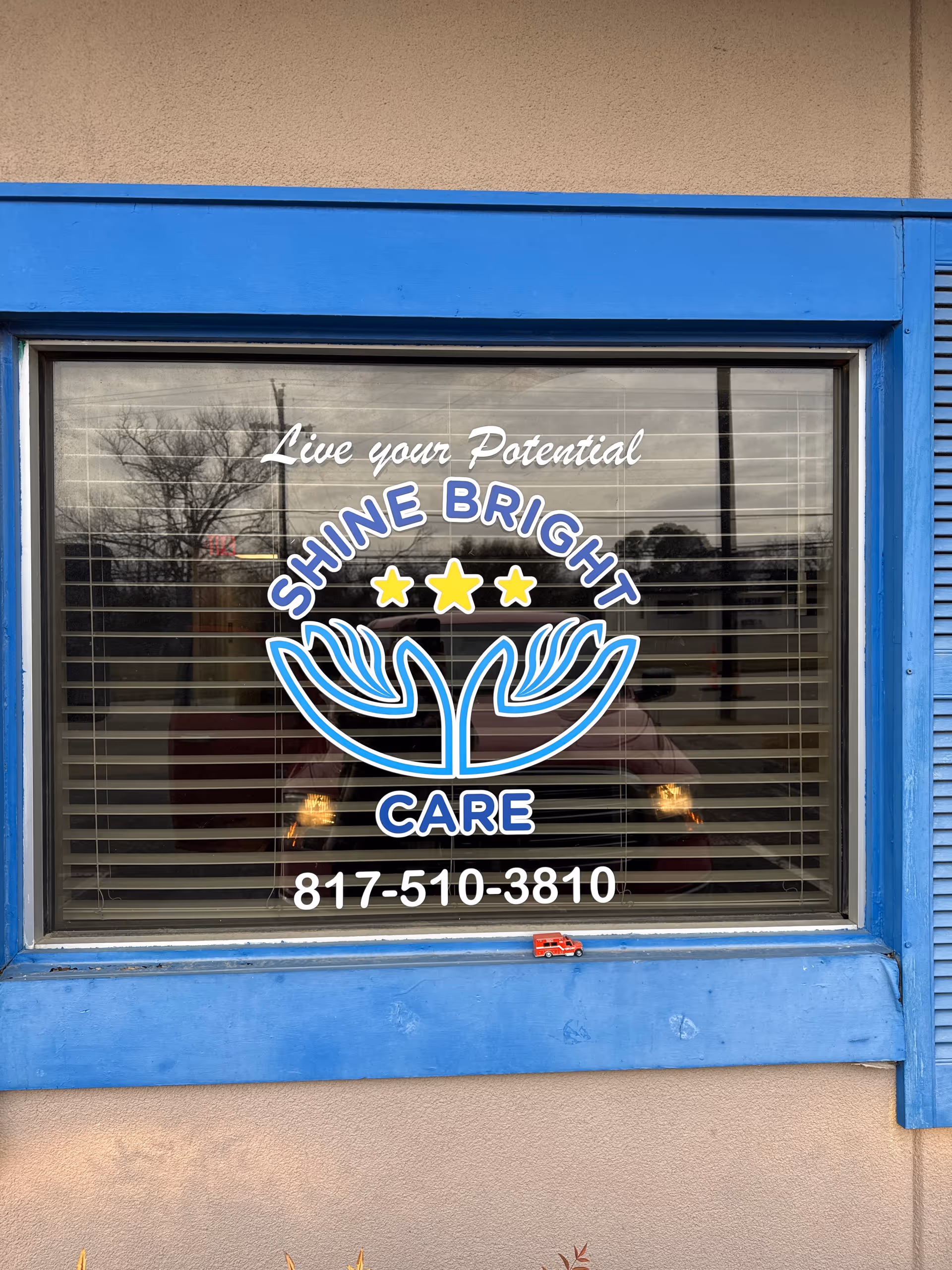 Blue-framed window on a building displays Shine Bright Care logo and phone number.