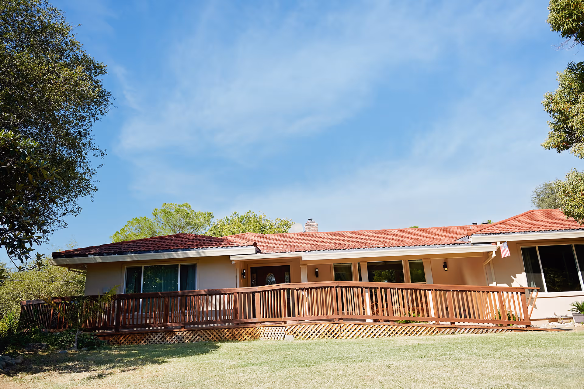 Single-story ranch-style building with a red tile roof, a wooden front ramp and a grassy yard under a blue sky.