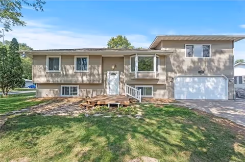 Two-story beige building with a front entrance, attached garage, and grassy lawn under a clear sky.