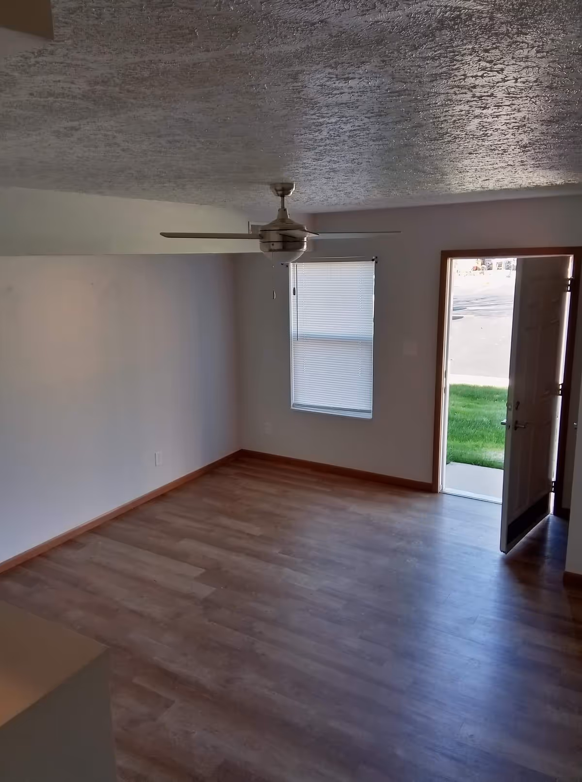Unfurnished Ashley Manor living room with ceiling fan, window, and open exterior door.