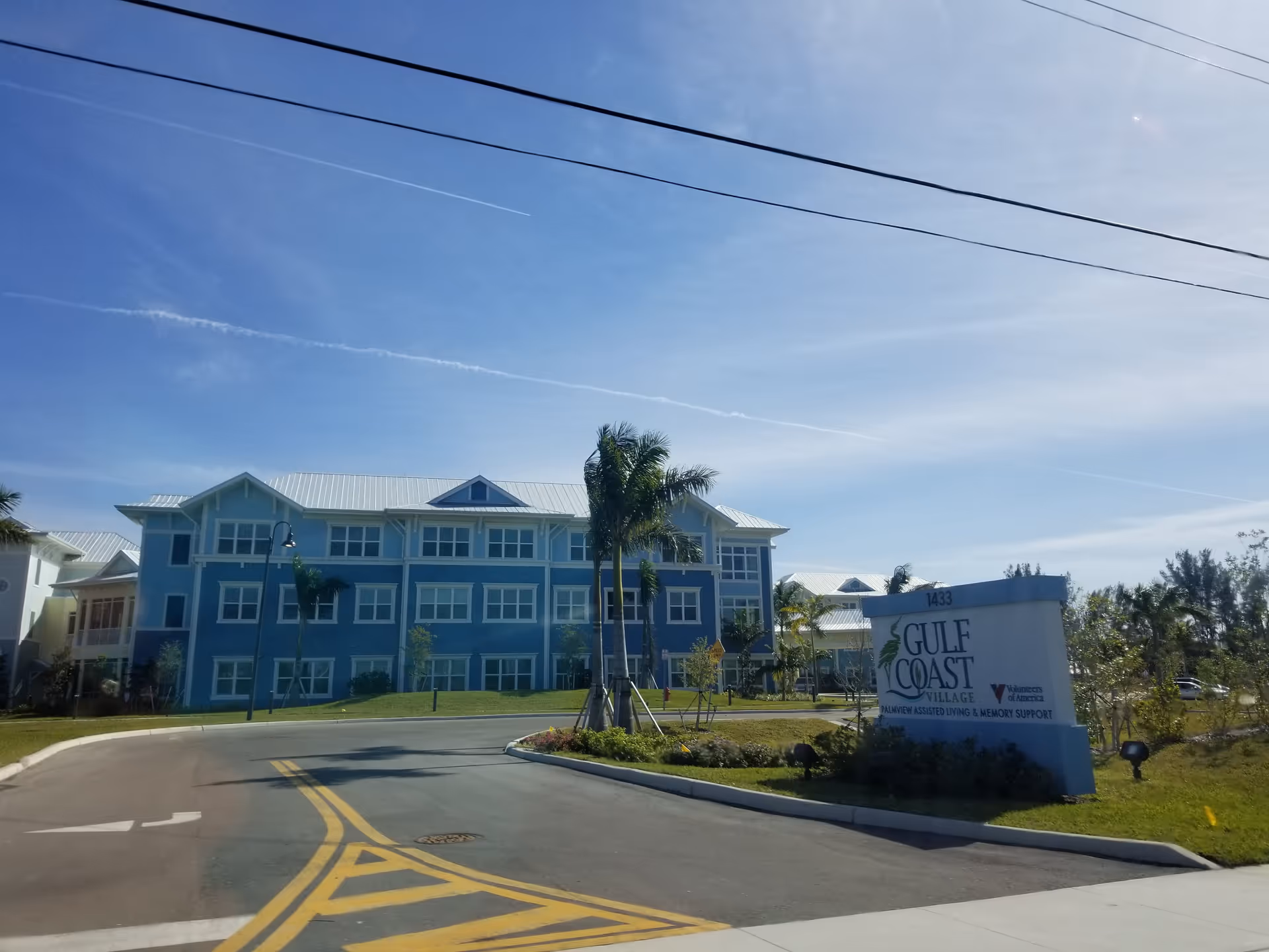 Blue multi-story senior living building with palm trees and a Gulf Coast Village sign at entrance.
