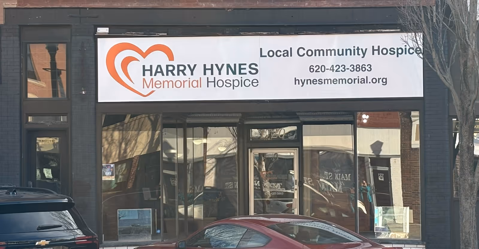 Exterior storefront of Harry Hynes Memorial Hospice with glass doors and parked cars.