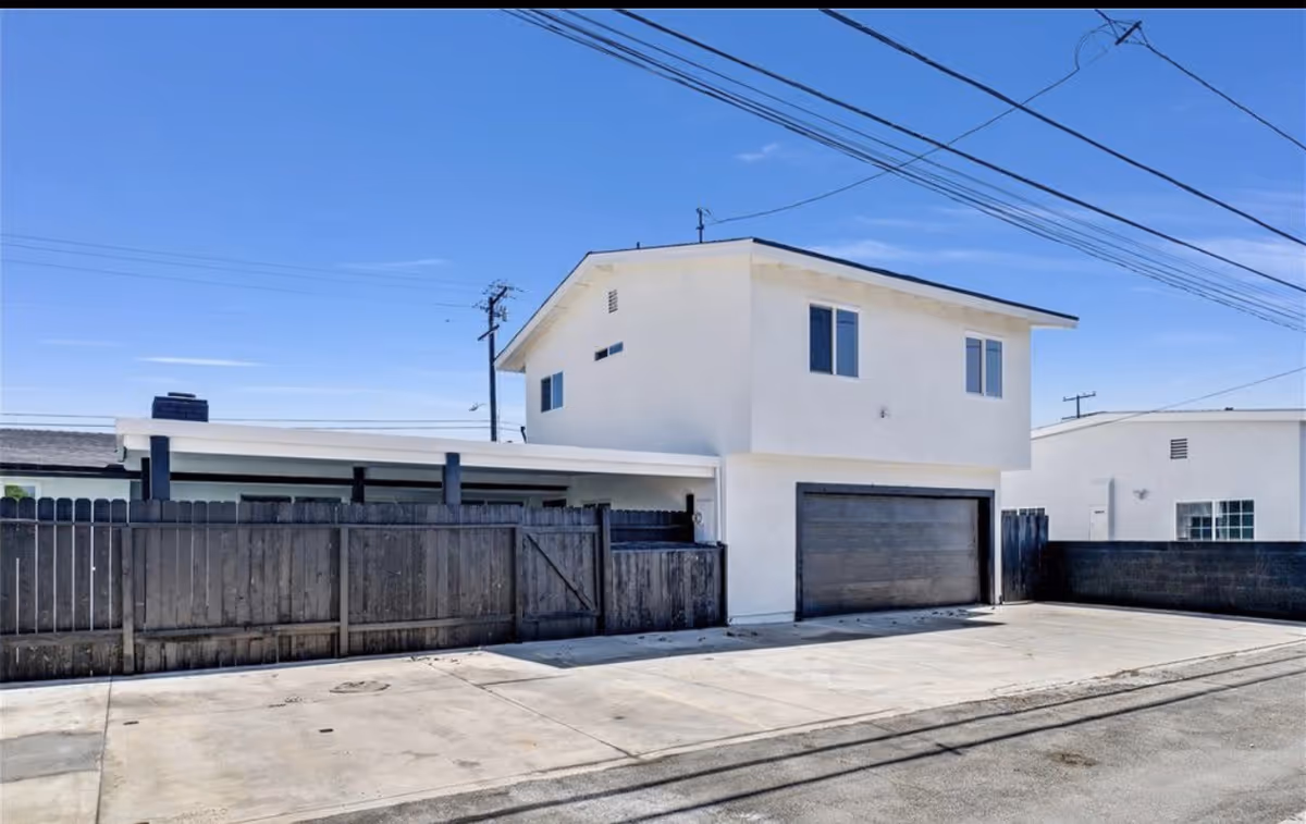 White two-story residential building with a metal garage door, fence, and clear blue sky.