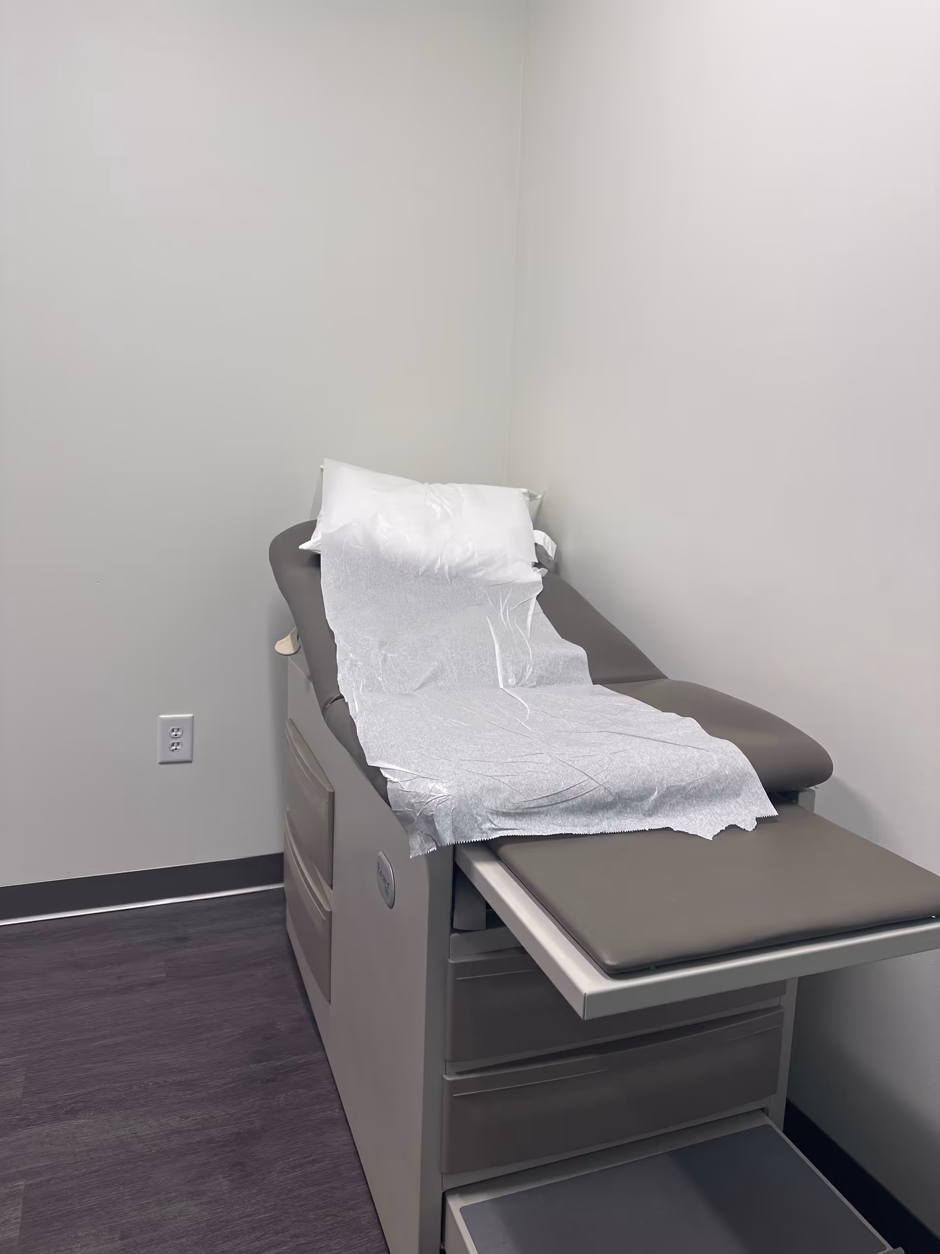 Examination chair in a small medical room with disposable paper sheet.
